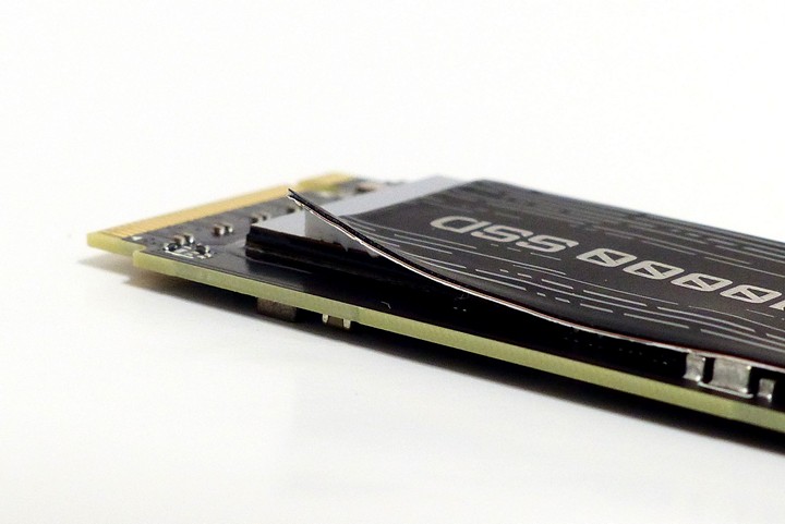 輕輕掀起 AORUS Gen5 10000 SSD 面貼紙一角，可以發現該貼紙由 3 層材料組成，由外而內分別是散熱用奈米碳塗層、導熱用金屬銅、固定用導熱貼。
