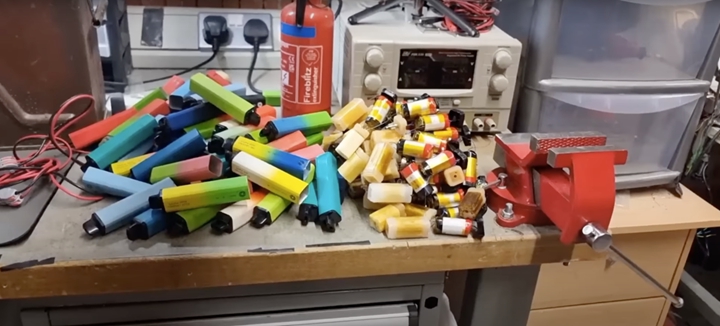 一堆空的鋁製電子菸外殼，以及從中取出的菸油和電池，放在克里斯·多爾的工作台上。 