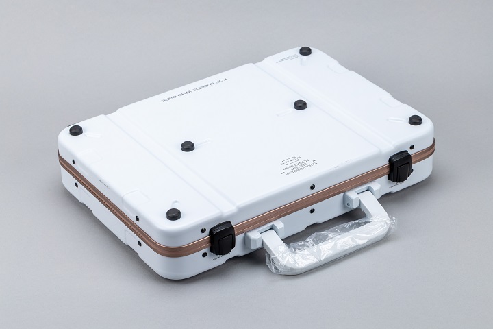 量身打造的手提箱採用純白色調，側面嵌入 Decennium Gold 金屬邊框，四周設有稜角分明的防護線條與技術噴印文字，營造出極致的精密裝備氛圍。